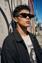 Model wearing DASH sunglasses in black frame with black lenses, portrait against a mural wall in LA arts district