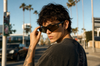 Model wearing DASH sunglasses in black frame with black lenses, candid pose with palm trees in Los Angeles