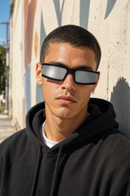 Model wearing PHANTOM sunglasses in black frame with mirrored lenses against a stucco wall in LA