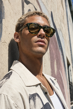 Model wearing SOLARIS sunglasses in green tortoise frame with gold hardware, arts-district alley lifestyle photo
